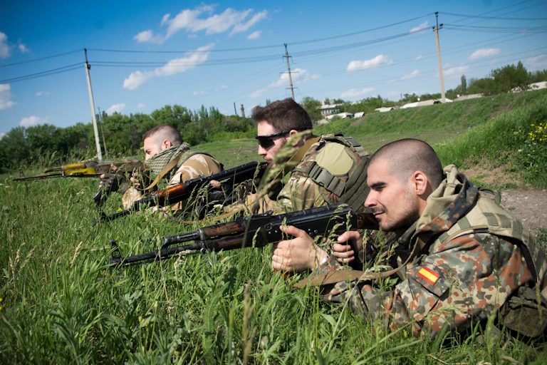 Three people in camouflage clothes lie on the ground pointing rifles