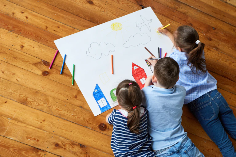 Trois enfants dessinent sur une grande feuille de papier