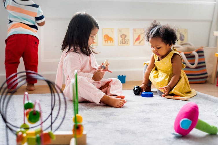 Two toddlers seen sitting on the floor in an early learning and care centre.