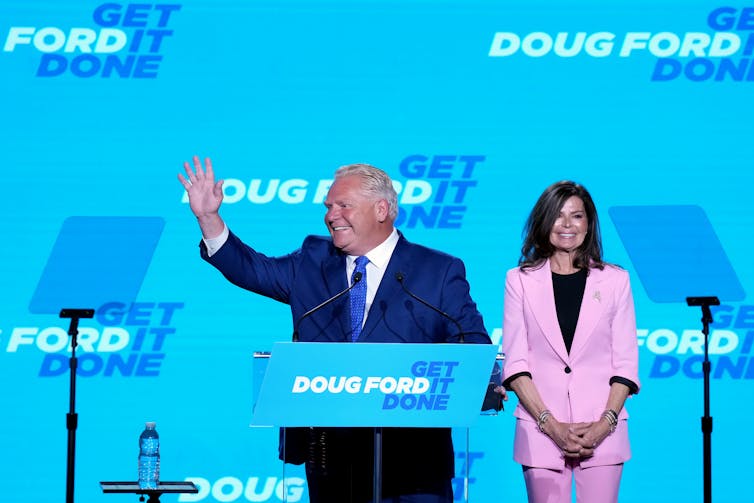 A man in a suit waves from behind a podium