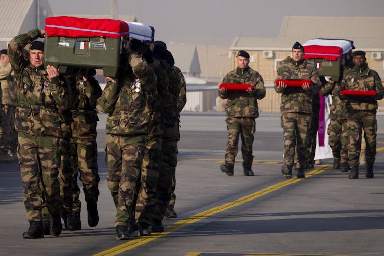Soldiers carry coffins draped with the French flag