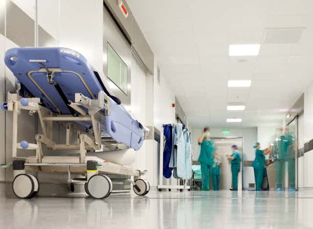 An empty gurney in the foreground of a hospital corridor, with people in scrubs out of focus in the background