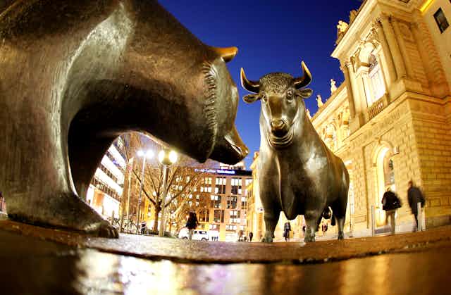 A bronze statue of a bear stands in front of a bronze statue of a bull at night in front of city buildings