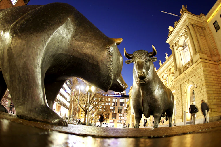 A bronze statue of a bear stands in front of a bronze statue of a bull at night in front of city buildings