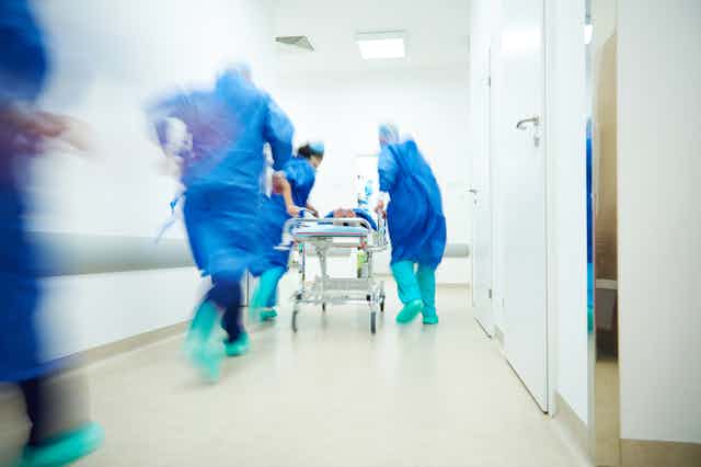 Hospital staff pushing trolley fast along hospital corridor