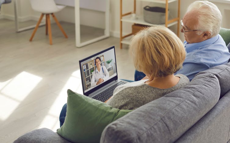 Older couple sitting on sofa during telehealth appointment with doctor or screen