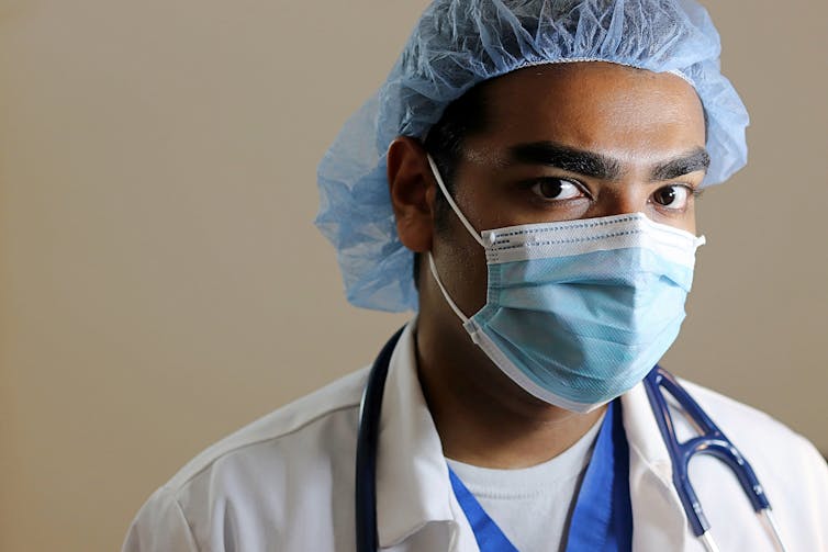 A medical worker in protective gear and and scrubs looks at the camera.