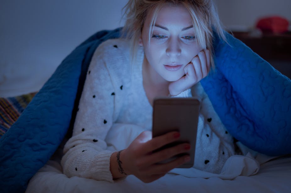 Woman looks at her phone in bed