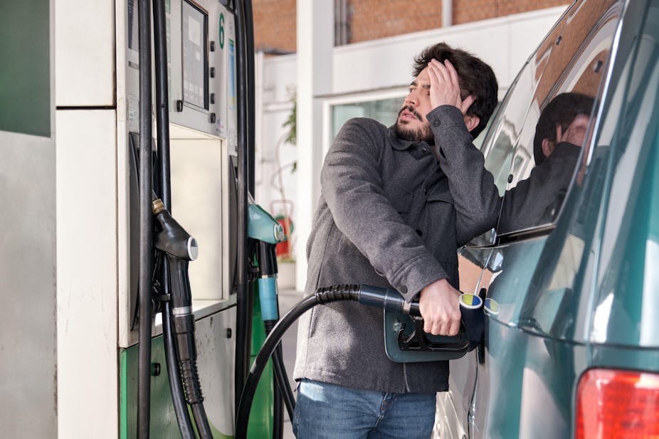 Man filling his car at the pump and looking worried