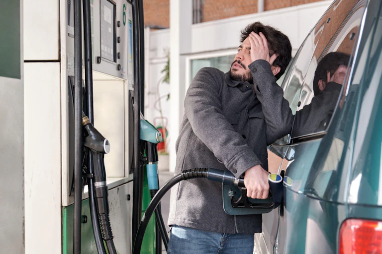 Man filling his car at the pump and looking worried