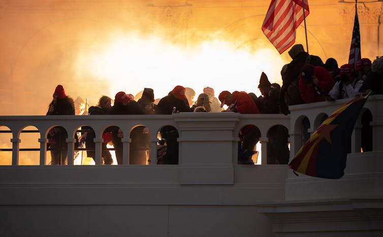 Supporters of President Trump storming the US Capitol, illuminated by a flare behind them.