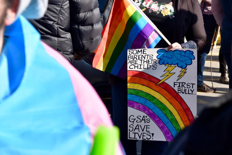 A sign at a rally with a rainbow is seen that says some parents are their child's first bully.