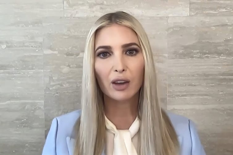 A woman with blond and dark hair in a blue jacket and white shirt, talking.