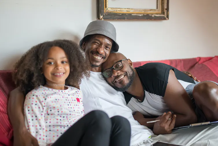 Two fathers seen with their daughter on a couch.
