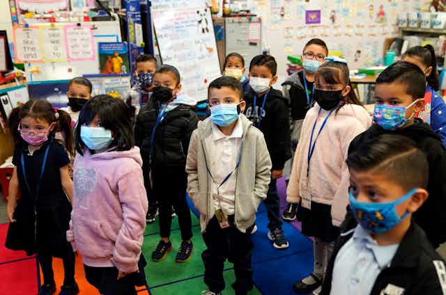 Children wearing masks stand in a classroom