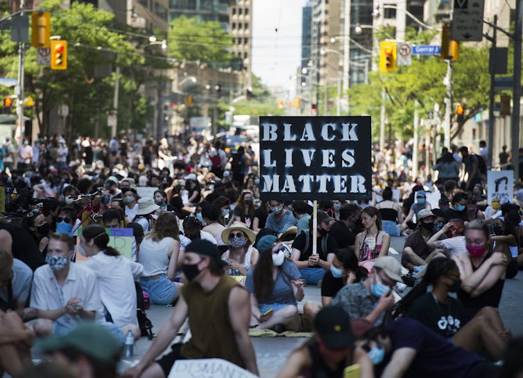 people sitting in the street with a BLACK LIVES MATTER sign