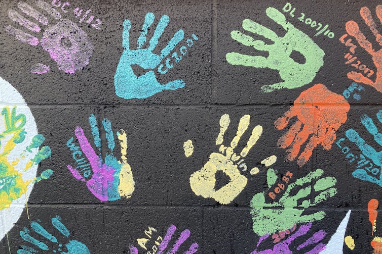 A black wall with colourful handprints and names on it