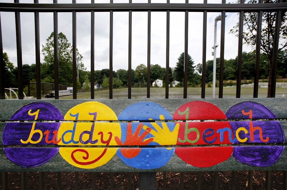 Five colored circles that say 'buddy bench' displayed on a school bench.