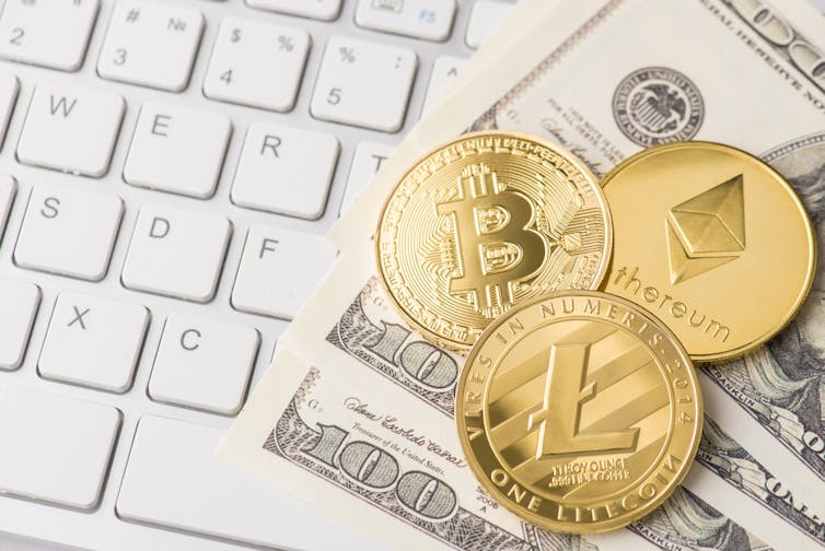 Photo rapprochée de pièces de monnaie dorées de bitcoin, ethereum et litecoin couchées sur du papier monnaie américaine et clavier blanc