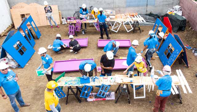 People in hard hats paint the parts of a colorful house.