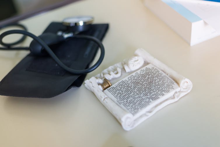 A black blood pressure gauge sits on a table next to a small white tablet with writing on it.