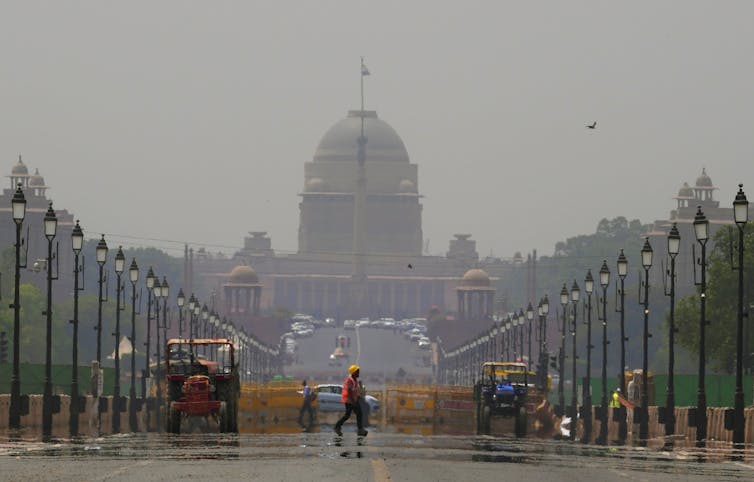 A construction worker walks across a mirage on the road in front of a historical building