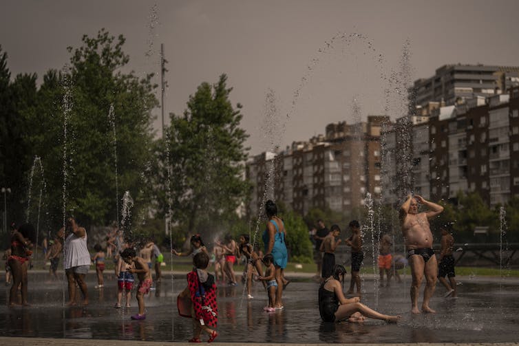 Children and adults cool off in fountain in a park