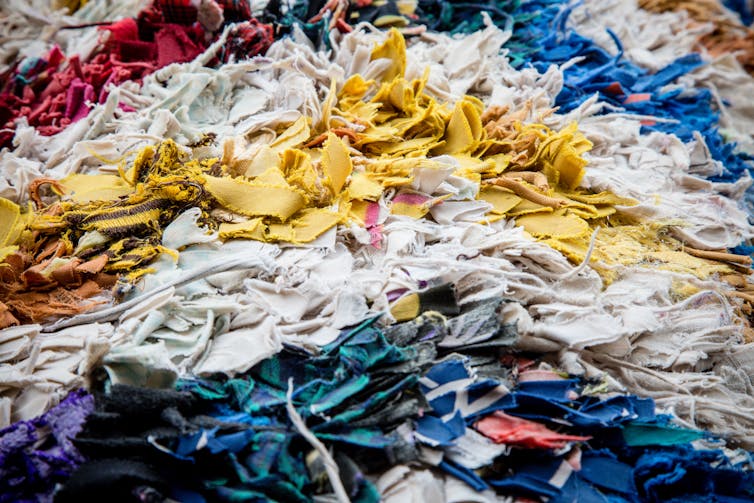 Massive amounts of clothing scraps are stacked on top of each other, loosely sorted by colour.