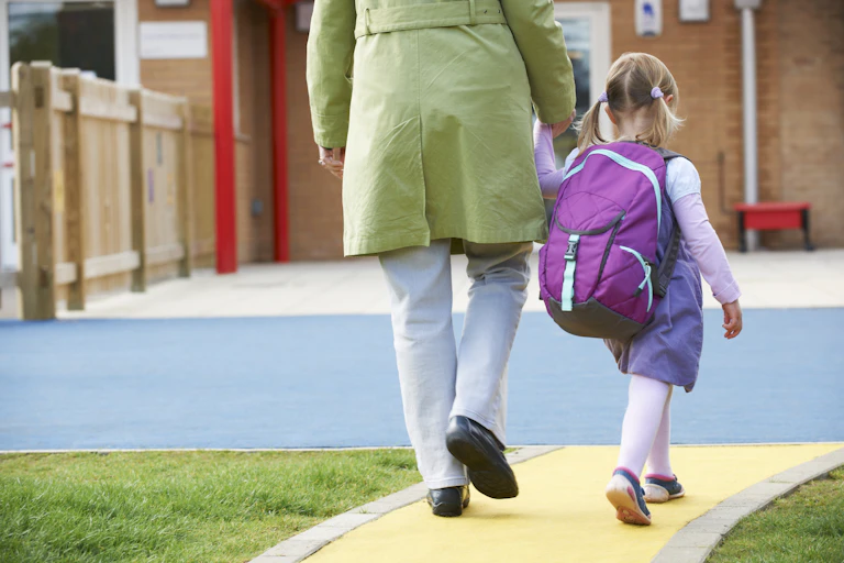 Woman holds the hand of a small girl as they walk to preschool