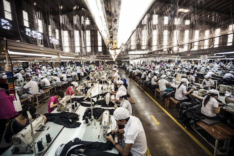 Rows of workers operate sewing machines inside a factory hall