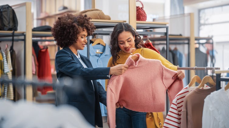 Two people look at a pink sweater in a store