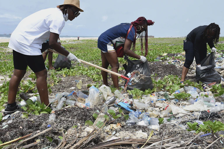 A man and two women packing trash into bags on the beach.