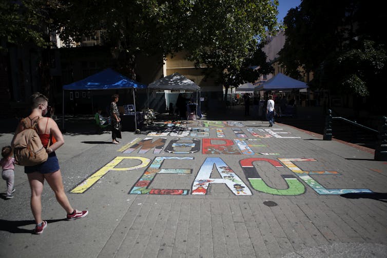 People are looking at a mural painted on the ground that reads More Justice More Peace.