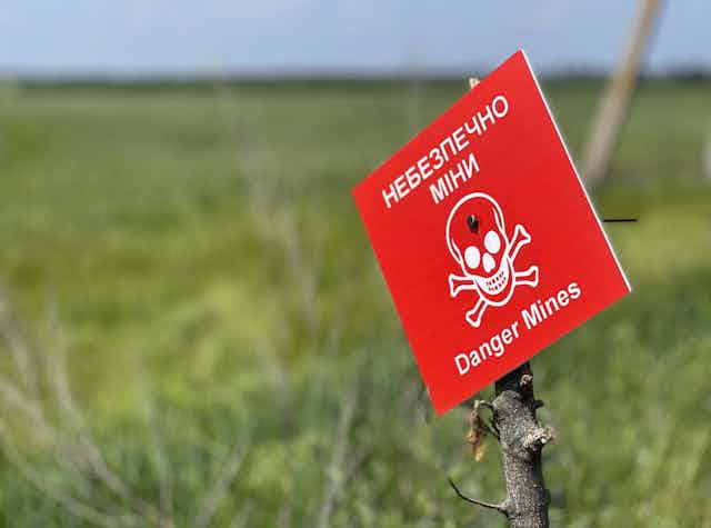 A photo showing a red sign with a skull and crossbones reading "Danger Mines" in English and Ukrainian.