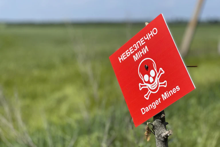 A photo showing a red sign with a skull and crossbones reading "Danger Mines" in English and Ukrainian.