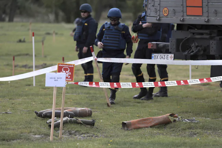 Men in protective gear in a field with unexploded land mines.
