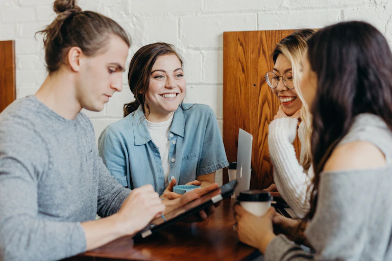 Students chatting at a table while one looks at a tablet