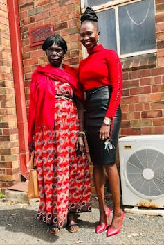 Two women stand in front of red-brick building, smiling together.