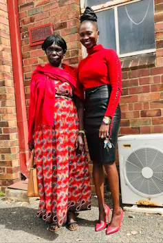 Two women stand in front of red-brick building, smiling together.