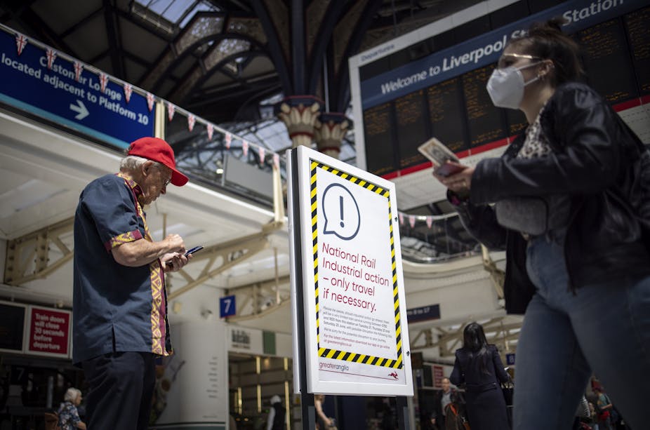 Man in red cap and woman with mask walk past a poster alerting travellers to national rail industrial action