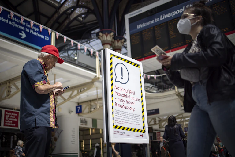 Man in red cap and woman with mask walk past a poster alerting travellers to national rail industrial action