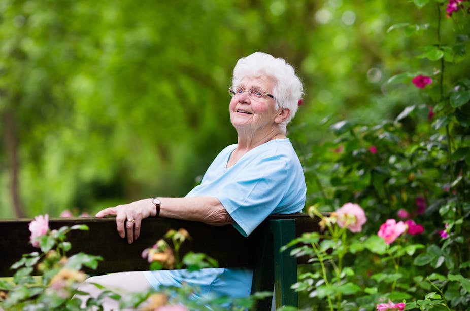 An elderly woman sitting on a bench in the garden looking happy.