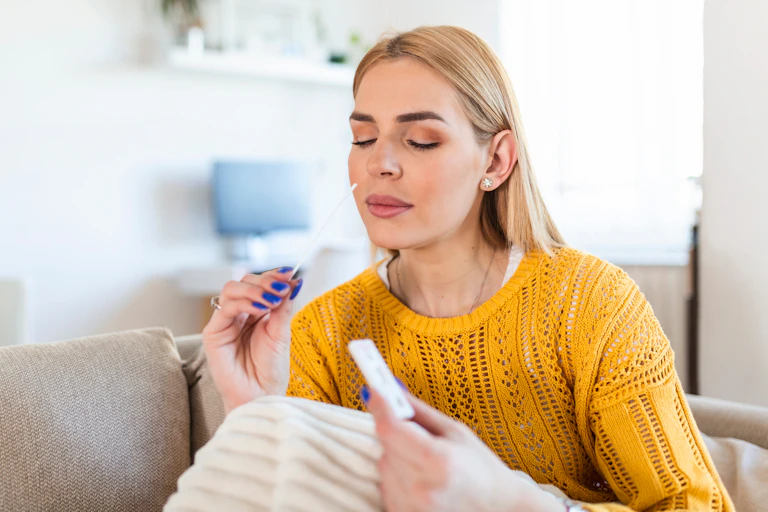 Young woman in yellow jumper gets ready to swab her nose.