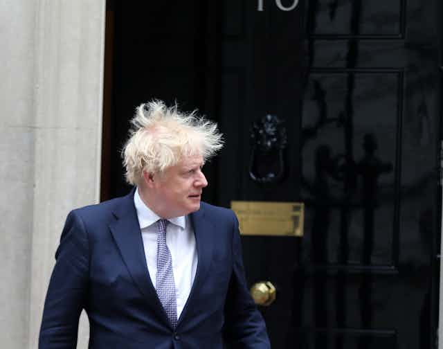 Boris Johnson outside of Number 10 downing street, looking to the left as his hair blows wildly in the wind