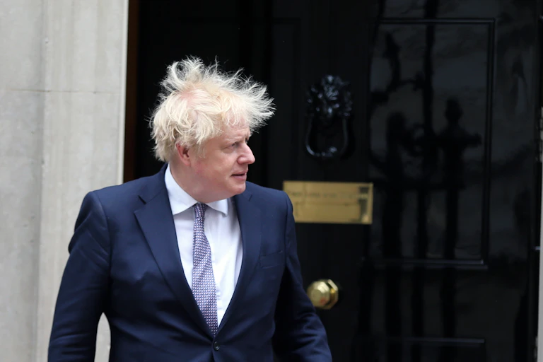 Boris Johnson outside of Number 10 downing street, looking to the left as his hair blows wildly in the wind