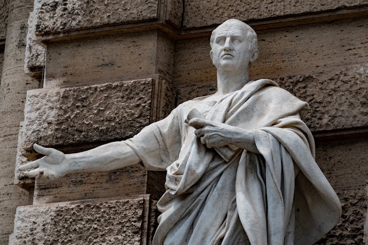 A marble statue of a Roman emperor with an arm outstretched.