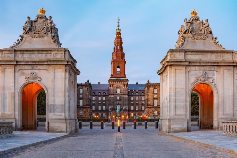 The ornate main entrance to Christiansborg with two Rococo pavilions on either side, against a pale blue morning sky in Copenhagen
