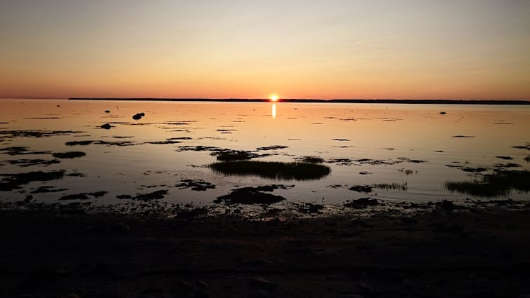 A sun sets low on the horizon over a body of water.