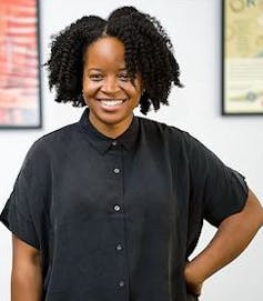 Woman poses in black shirt with one arm on hip.