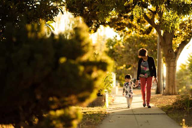 Parent and child walking down tree-lined sidewalk